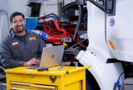 Technician next to truck typing notes on laptop