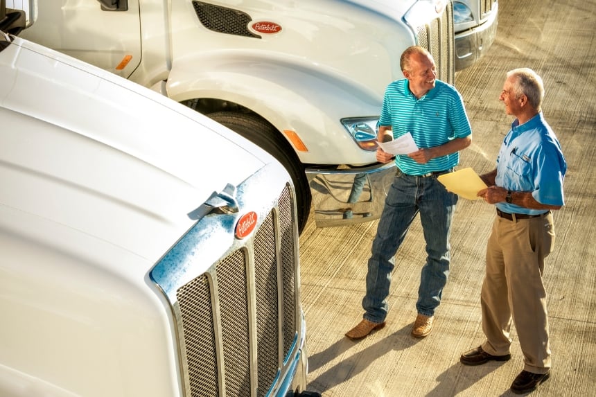 Two men holding papers next to truck